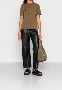 Camicia corta a maniche corte marrone con bottoni, pantaloni larghi neri in pelle, sandali neri con cinturino e una borsa tote verde oliva. Texture lisce.