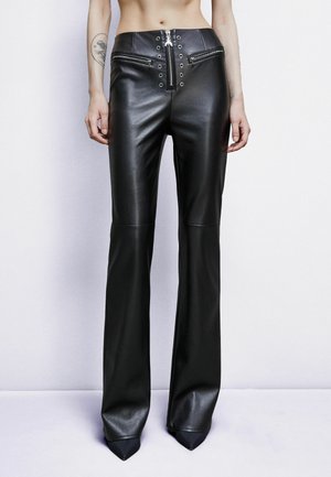 Pantaloni flare in pelle nera con vita alta, caratterizzati da zip metalliche e chiusure a scatto, texture liscia e dettagli appuntiti alle caviglie.