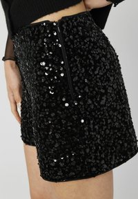 Shorts noirs en sequins présentant un design ajusté, une surface brillante avec de multiples sequins et une fermeture éclair discrète à l'arrière.
