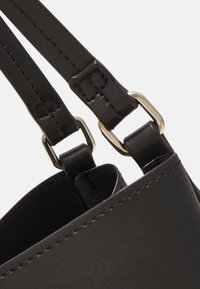 Sangles de sac en cuir noir avec boucles rectangulaires en métal argenté fixées au bord supérieur d'un sac en cuir noir.