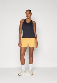 Débardeur noir sans manches, shorts jaunes, chaussettes blanches et sneakers clairs. Tissu lisse, coupe décontractée et design simple sans motifs.