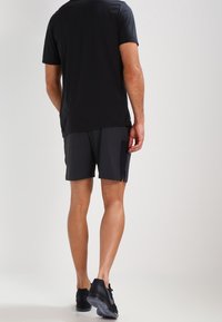 Černé sportovní tričko a šedé kraťasy. Lehký materiál odvádějící vlhkost. Obsahuje boční větrací otvory, krátké rukávy a elastický pas.