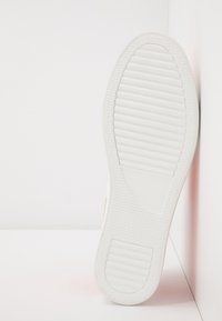 Semelle de sneaker blanche avec surface texturée, comportant une section verticale et des rainures horizontales pour l'adhérence, reposant sur un fond blanc.