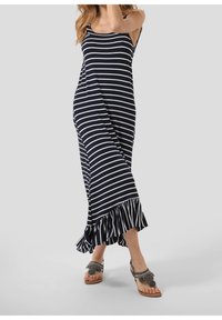 Robe maxi à rayures bleues marine et blanches avec des bretelles spaghetti, ourlet évasé avec des volants, assortie à des sandales plates décoratives.