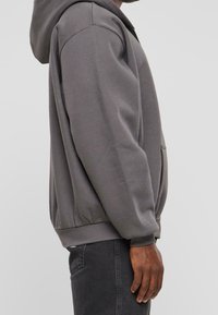 Sudadera gris con un bolsillo canguro, puños y dobladillo acanalados. Hecha de una suave mezcla de algodón, con un corte relajado y capucha con cordón.