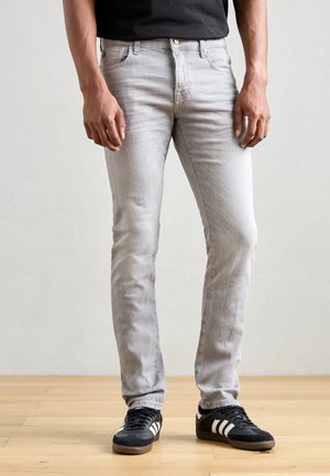 Light grey denim jeans with a slim fit, featuring classic five-pocket design, belt loops, and a button closure. Worn with black sneakers.