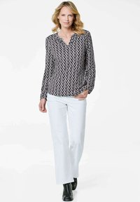 Blusa a maniche lunghe con scollatura a V, caratterizzata da un motivo geometrico in bianco e nero, abbinata a pantaloni bianchi e stivaletti neri.