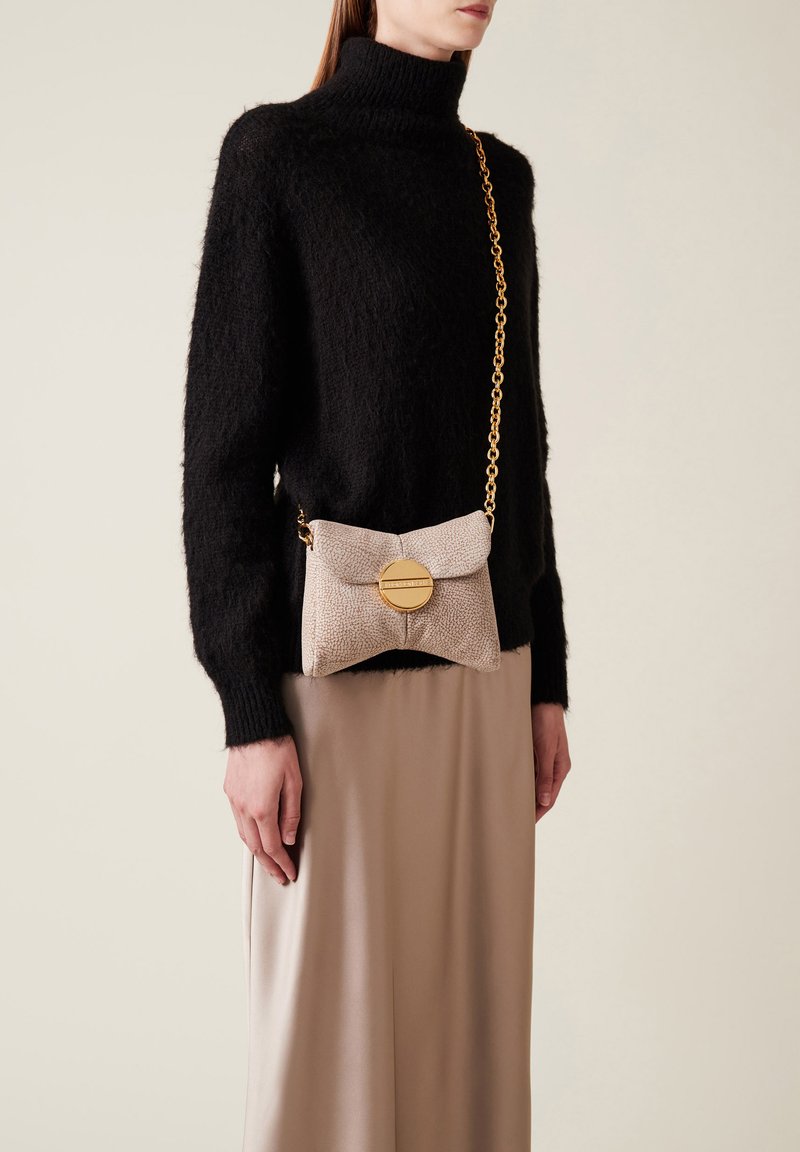 Beige Handtasche mit strukturiertem Material, einem runden goldenen Akzent und einer Kettenriemen.getragen zu einem schwarzen, flauschigen Rollkragenpullover und einem beigen Rock.