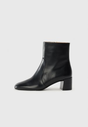 Bottine en cuir noir avec un bout pointu, une texture lisse et un talon carré block. Caractérisée par un design simple de couture latérale.