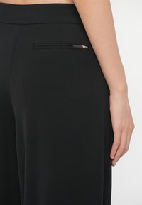 Κοντινό πλάνο ενός ατόμου που φορά μαύρο παντελόνι ψηλής μέσης με μικρή πίσω τσέπη και το δεξί του χέρι resting στο πλάι του.