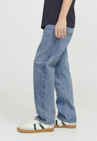 Jeans de mezclilla azul claro, de corte relajado, con costuras laterales y textura desgastada, combinados con zapatillas blancas con rayas verdes.