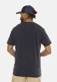 Camiseta de algodón gris oscuro con cuello redondo y mangas cortas, mostrada desde la parte posterior. Presenta un ajuste relajado y un diseño simple.