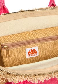 Sac en tissu rose, intérieur avec doublure beige, doté d'une poche zippée en brun avec un motif texturé et une étiquette blanche avec un logo orange.