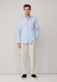 Camisa de botones azul claro con un bolsillo en el pecho, pantalones beige y zapatillas negras. Tela suave, mangas largas, diseño ajustado.