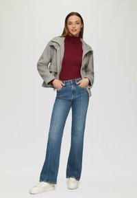 Grau melierte Wolljacke mit Druckknöpfen, bordeauxfarbener Rollkragenpullover und blauen Schlagjeans. Weiße Sneaker runden das Outfit ab. Sauberer, lässiger Stil.