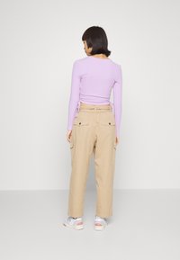 Camisola de manga longa em roxo claro, com detalhe franzido na lateral; combinada com calças cargo bege, com bolsos laterais e um corte descontraído.