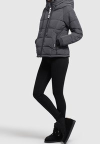 Doudoune grise avec capuche, poches zippées et poignets en tricot, associée à un jean noir ajusté et des bottes noires texturées.