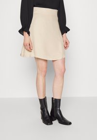 Saia A-line bege com uma textura suave, design de cintura alta e uma bainha fluida, combinada com botas de tornozelo pretas com biqueira quadrada e fecho de correr.