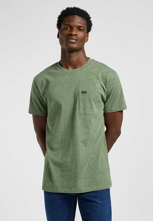 T-shirt verde a maniche corte con collo rotondo realizzata in tessuto a trama, dotata di una tasca sul petto sinistro e di un piccolo etichetta del marchio vicino alla tasca.
