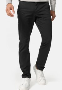 Black trousers with a slim fit, made from a smooth, lightweight fabric. Features a classic design with a zip fly and side pockets.