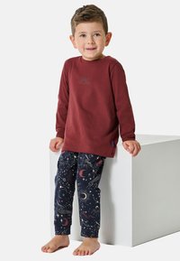 Langärmliges bordeauxfarbenes Hemd mit einem Sonnendesign, kombiniert mit marineblauen Hosen, die himmlische Muster aus Sternen, Monden und Spiralen aufweisen.