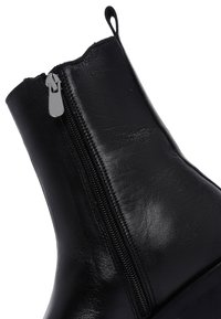 Bottines en cuir noir à finition brillante, avec fermeture éclair sur le côté et languette de tirage, conçues avec une forme ajustée et élégante.