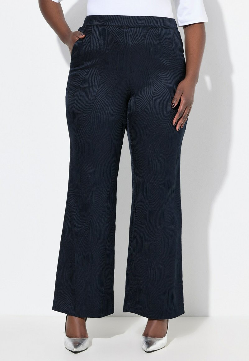 Marineblaue Schlaghosen mit einem strukturierten, wellenförmigen Muster, ausgestattet mit einem breiten Taillenbund und seitlichen Taschen, kombiniert mit silbernen High Heels.