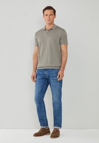 Polo gris de manga corta, jeans azules y zapatos de ante marrón. El polo tiene un cuello y un dobladillo recto; los jeans son ajustados.