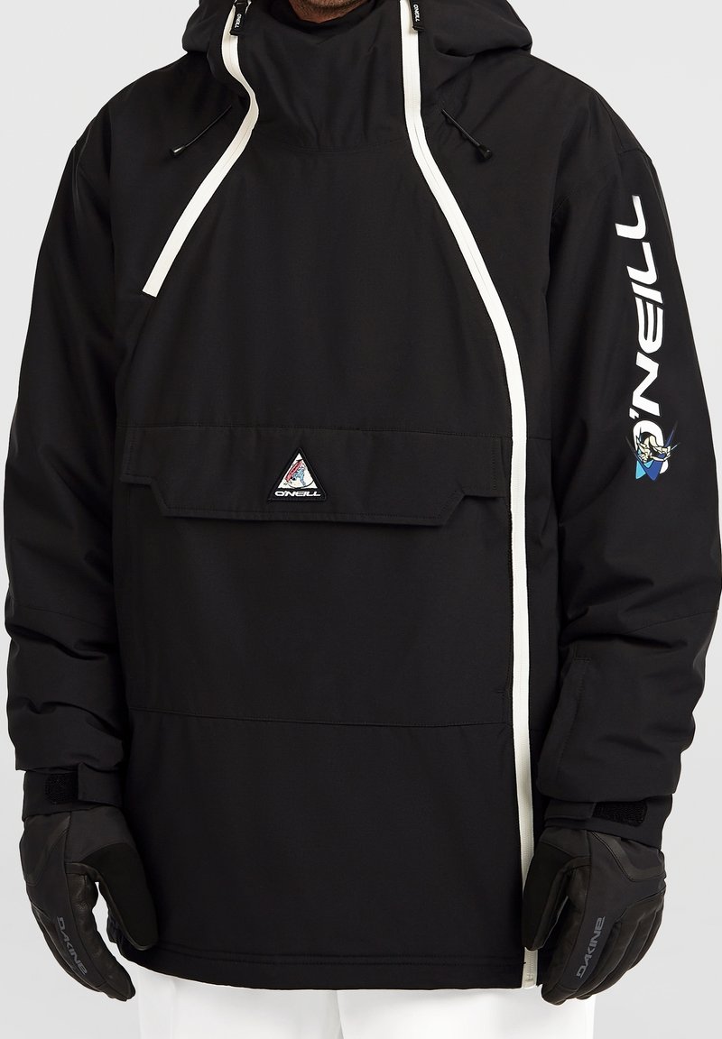 Homme portant une veste à capuche noire O'Neill avec des détails de fermeture éclair blancs et un logo sur la manche, associée à des gants noirs et un pantalon blanc.