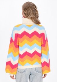 Kleurrijke zigzagpatroon trui van zachte brei, met tinten roze, geel, blauw en crème. Hoge hals en oversized mouwen.