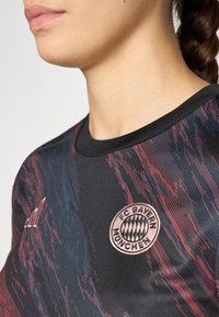 Zwart shirt met gestructureerde rode en blauwe diagonale strepen, geribbelde kraag en het FC Bayern München-logo in het roze. Adidas-logo op de mouw.