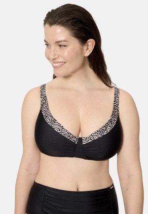 Mujer sonriendo, con un top de bikini negro con ribete claro con estampado y braguitas de bikini a juego de talle alto, de pie contra un fondo liso.