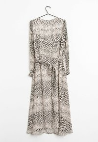 Langärmliges Midikleid mit beigem und schwarzem abstraktem Punktmuster, mit einem gebundenen Taillengürtel, der an einem schwarzen Kleiderbügel vor weißem Hintergrund hängt.