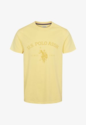 Sárga pamut póló kerek nyakkal, nagy, tónusos U.S. Polo Assn. logóval és egy lovon polo játékost ábrázoló grafikával.