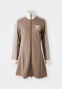 Brun Adidas-jacka med hög krage och hel dragkedja. Har tre vita ränder på ärmarna och en broderad logga på bröstet.