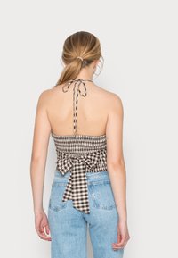 Top halter de quadros castanhos e brancos com um design franzido e um laço na parte de trás, combinado com jeans de cintura alta azuis claros.