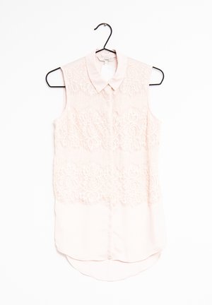 Różowa bluzka bez rękawów z koronkowym wykończeniem, kołnierzykiem i zapięciem na guziki. Posiada zaokrąglony dół i miękką teksturę materiału.