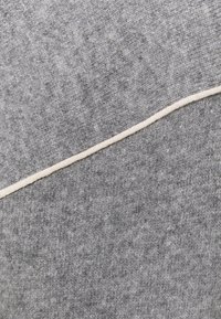 Szary dzianinowy sweter ma diagonalną fakturę. Jasnoszare akcenty ściegów oddzielają dwa różne odcienie szarości. Miękka, teksturowana powierzchnia.