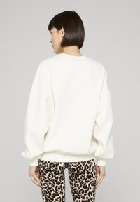 Balts džemperis ar nolaistām pleciem un ribotām aprocēm, kopā ar leoparda raksta legingiem. Mīksta tekstūra un brīvs piegriezums.