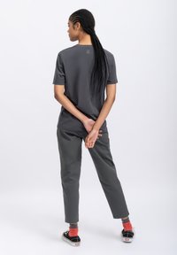 Grijze shirt met korte mouwen met een minimalistisch ontwerp, gecombineerd met grijze broek en zwarte schoenen. Vlecht haar naar achteren gestyled.