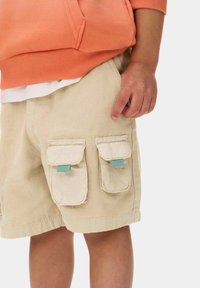 Beiga cargoshorts av texturerat tyg, med två framfickor med klaffar och blå detaljer. Styld med en orange hoodie.