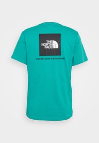 Camiseta de algodón color azul verdoso con mangas cortas. En la parte posterior presenta un gráfico cuadrado negro con el logo de "THE NORTH FACE" y el texto "NEVER STOP EXPLORING".