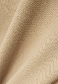 Beige cotton fabric with a fine diagonal texture, showcasing smooth surface and subtle sheen. Gentle folds create depth and dimension.