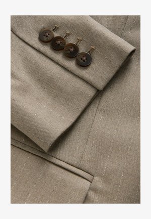 Bežový sak s upravenými rukávmi, na ktorých sa nachádzajú štyri tmavé gombíky, jemné pruhy a textúrovaná tkanina s viditeľným švom.