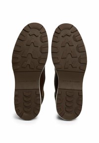 Hnědé gumové podešve s texturovaným vzorem, které mají bílý okraj a na povrchu je lisovaná značka "TOMMY HILFIGER".