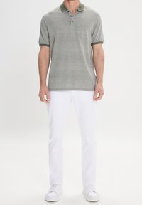 Polo de manga corta en gris claro con un patrón texturado, cuello verde oscuro y un bolsillo, combinado con jeans blancos y zapatillas blancas.