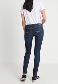 Smala blå jeans med hög midja, bakre yoke-detalj och två bakfickor. Parat med en vit T-shirt och svarta sneakers.