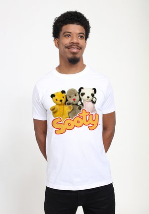 Hvid t-shirt med tre puppete karakterer: en gul bjørn, en grå bjørn og en sort-hvid panda, med ordet "Sooty" i orange bogstaver.