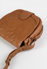 Brun læder crossbody taske med klaplukning, afrundet form, synlige syninger og justerbar rem. Glat tekstur med diskret mønster.