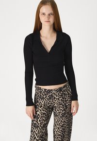 Crna rebrasta majica s dugim rukavima i ovratnikom, uparena s bež širokim hlačama s leopard uzorkom koje imaju kopčanje na gumbe i prednje džepove.
